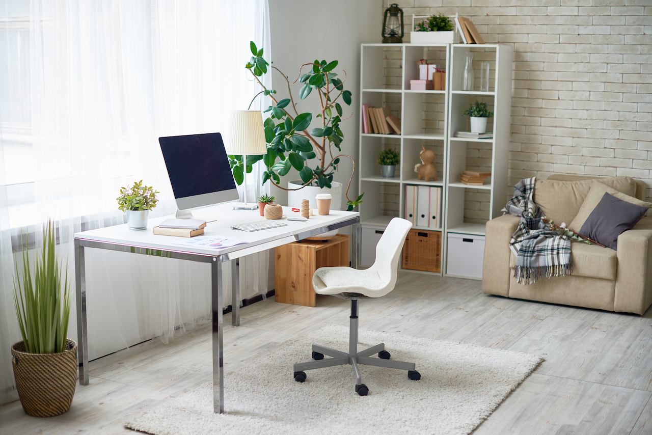 bright-lit home office space with desktop computer, bookshelf, and sitting chair.