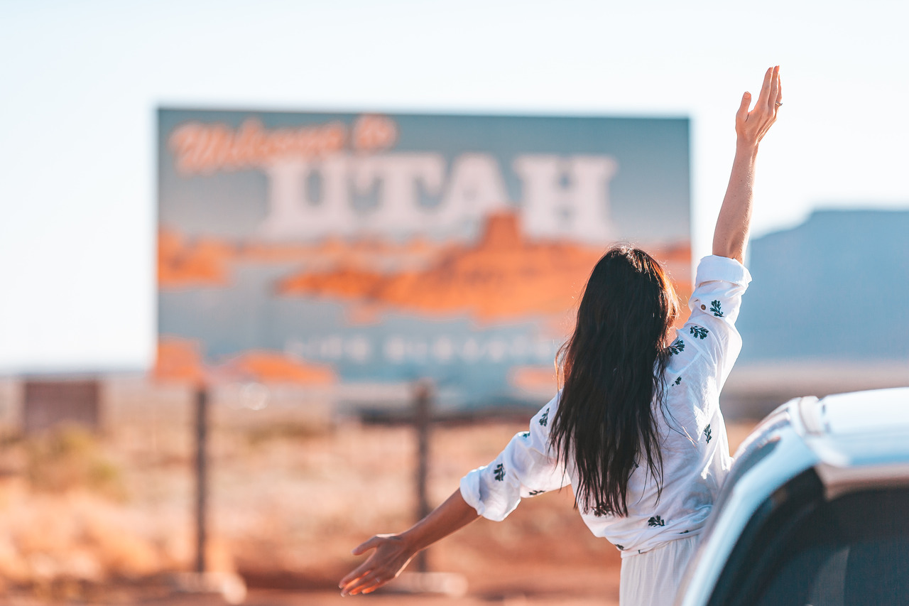 Car by the Utah State sign—people moving to Utah