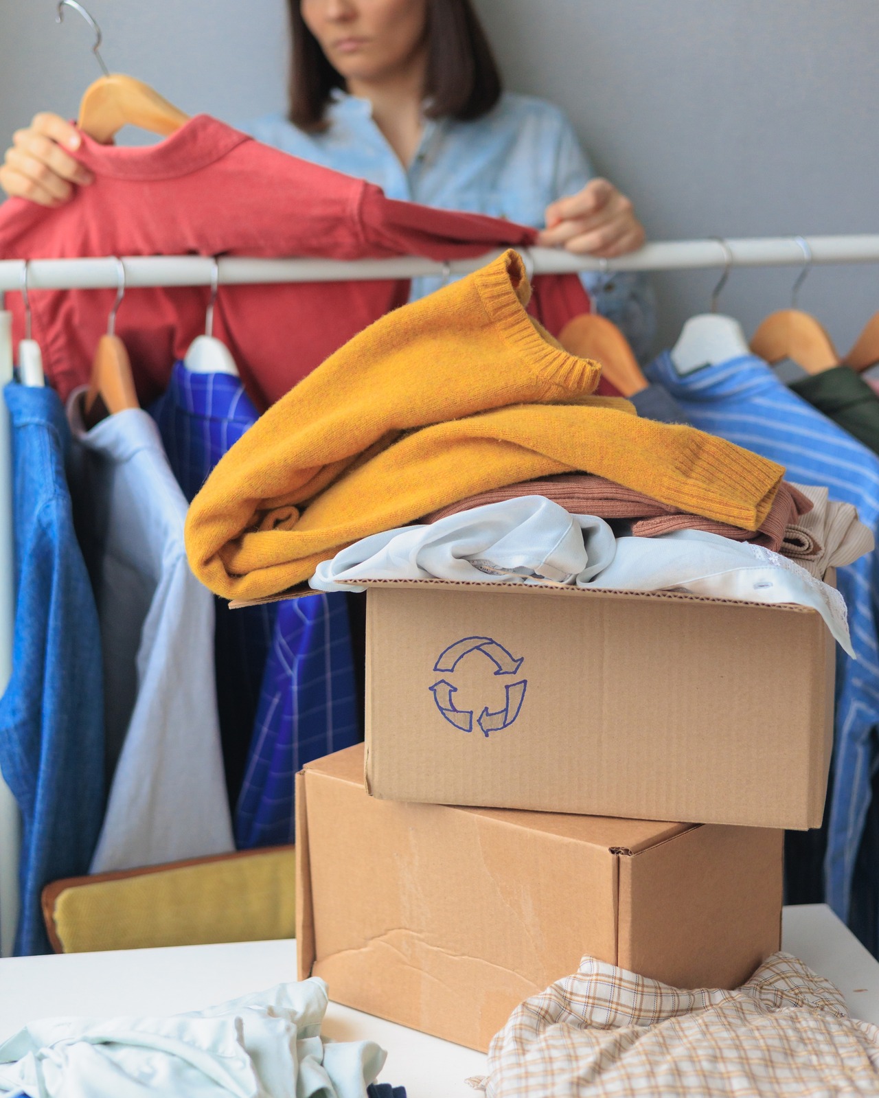 A woman sorts clothes on a hanger into a donation box